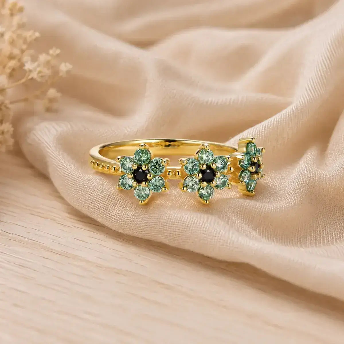 Anel de prata 925 banhada a ouro visto de lado com três flores em moissanite numa mesa de madeira posicionado de lado