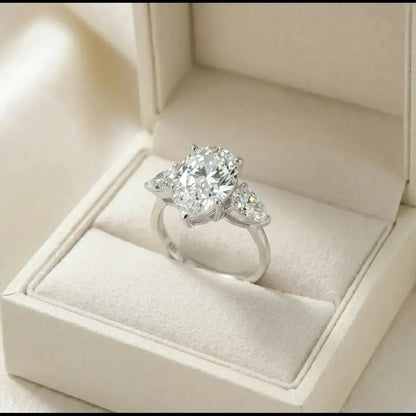 Anel de prata com pedra em formato de gota moissanite, em uma caixa minimalista de cor creme sobre tecido de seda