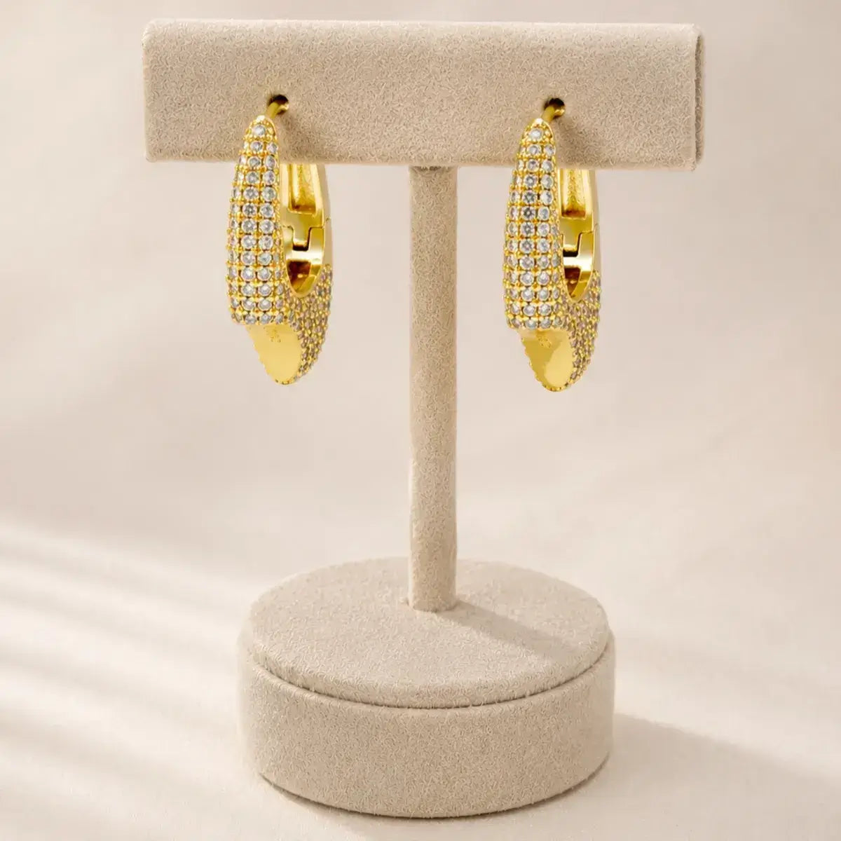 Brincos de argola assimétricos dourados em Prata de Lei 925 com pavé de zircónias  expostos num suporte de joias