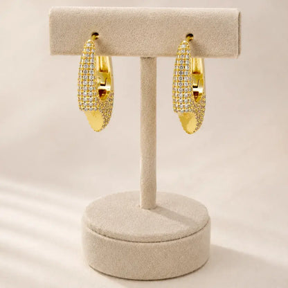 Brincos de argola assimétricos dourados em Prata de Lei 925 com pavé de zircónias  expostos num suporte de joias