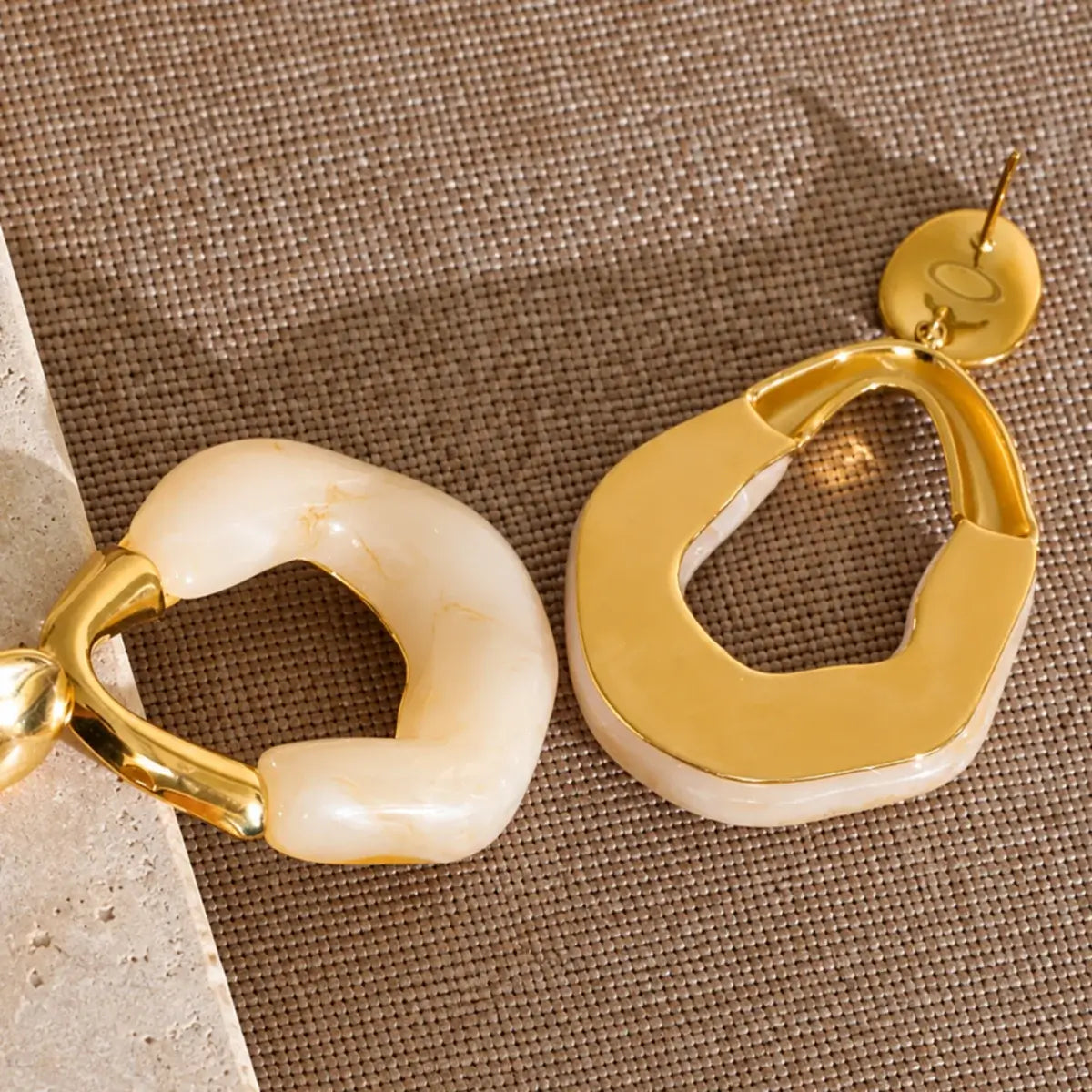 Brincos de resina bege com design geométrico e acabamento dourado visto parte de tras