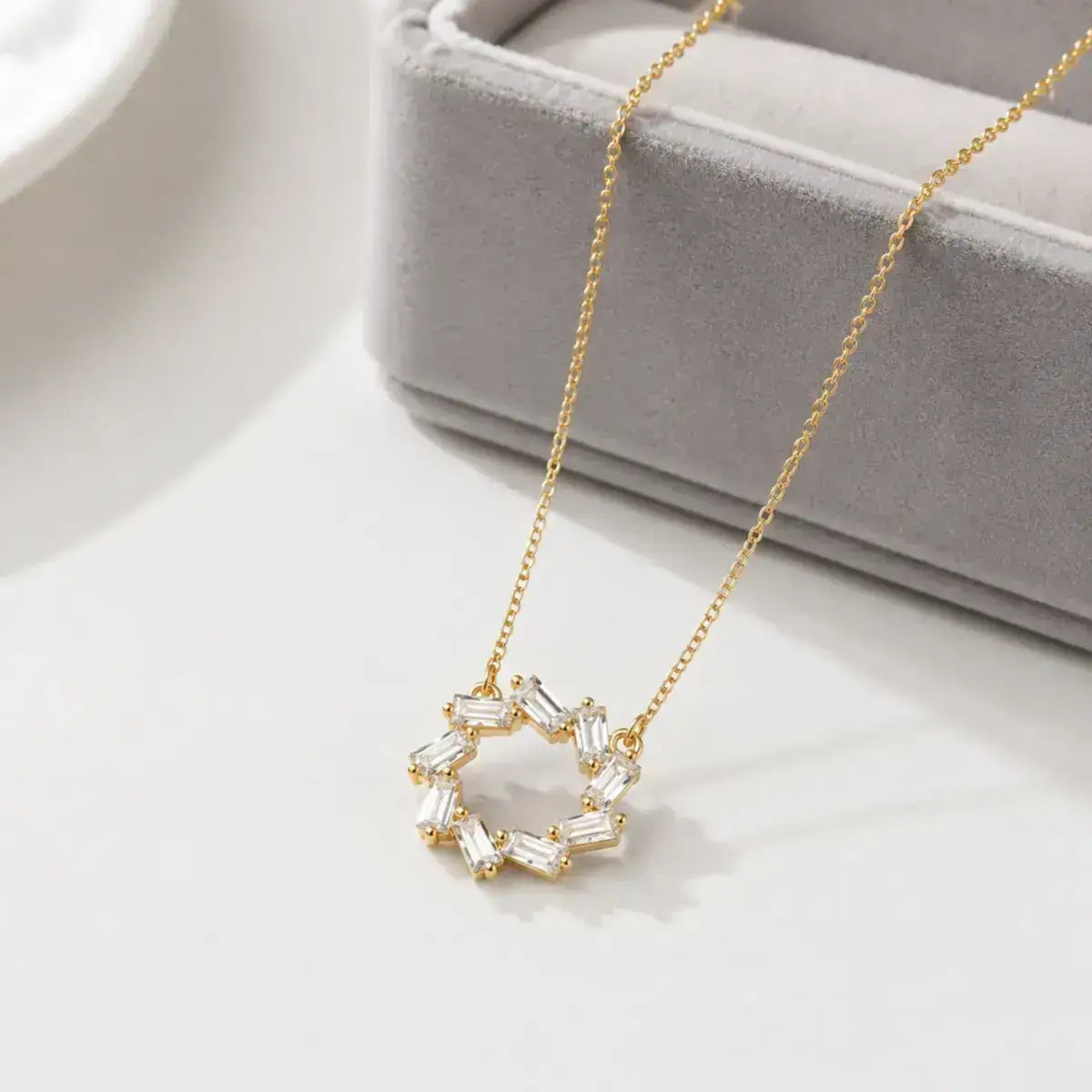Colar em Prata de Lei 925  dourado com pendente circular de zircónias baguete em cima da caixa de joias cinzenta e elegante