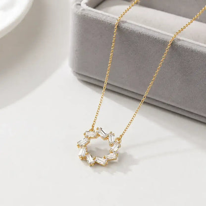 Colar em Prata de Lei 925  dourado com pendente circular de zircónias baguete em cima da caixa de joias cinzenta e elegante