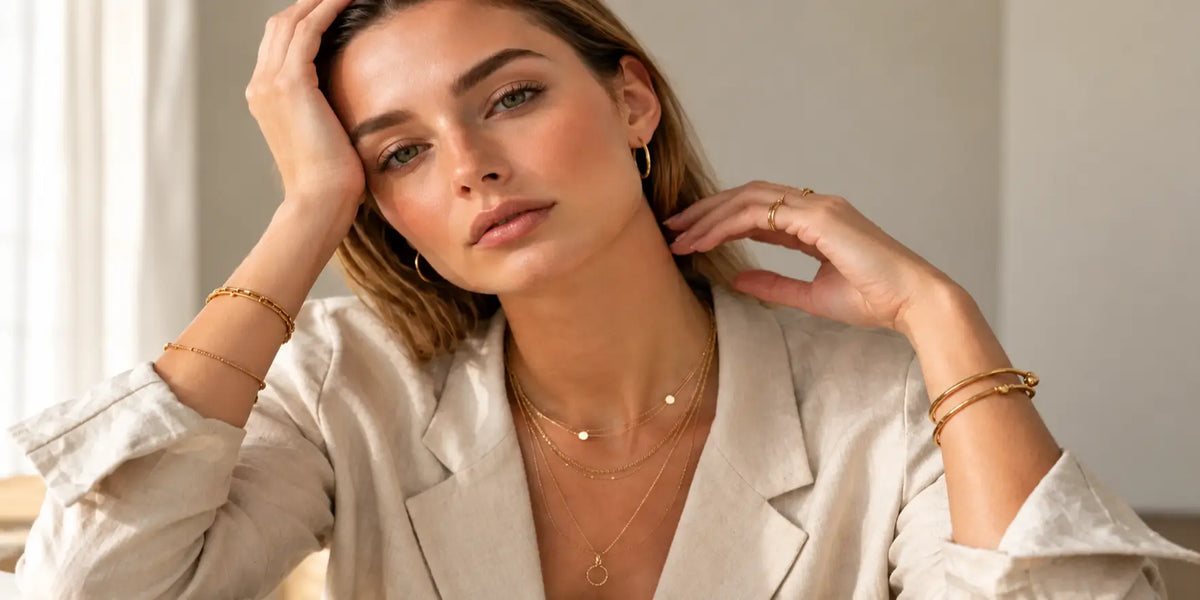 Modelo com colares dourados em camadas, pulseiras e anéis delicados, num look elegante e intemporal representando coleção Mais Vendidos da Vunelle.