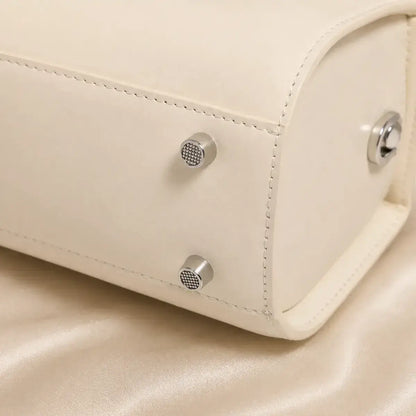 Detalhe da base com apoios metálicos da mala de mão em pele genuína Élise off white