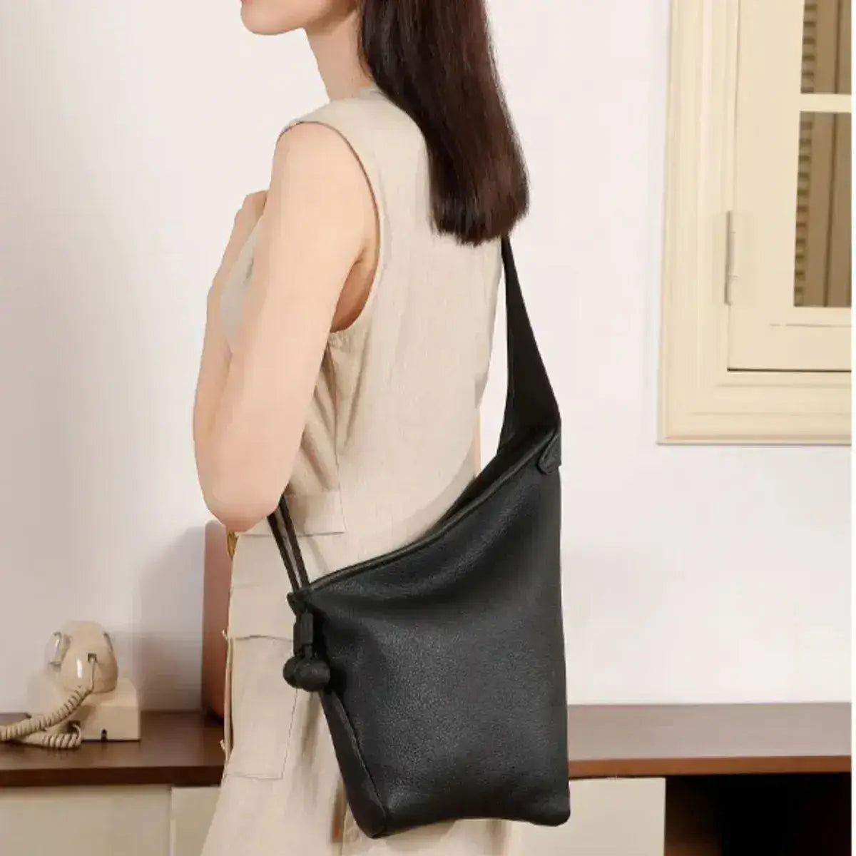 Modelo a usar a mala saco Aurora preta em pele genuína como tiracolo num look minimalista e sofisticado.
